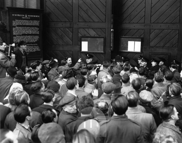 A black-and-white photograph of a large crowd of people gathered outside the gates of a prison.